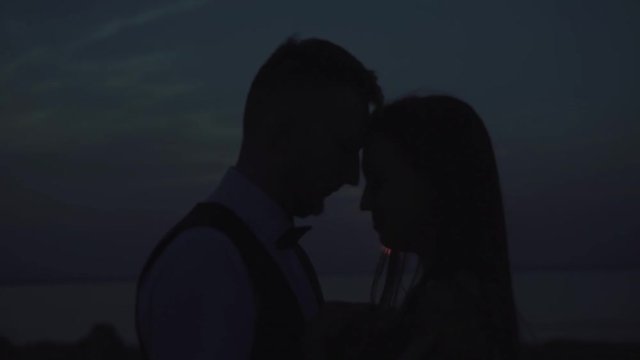 loving couple - young groom and beautiful bride at sunset and have hugs , silhouette view