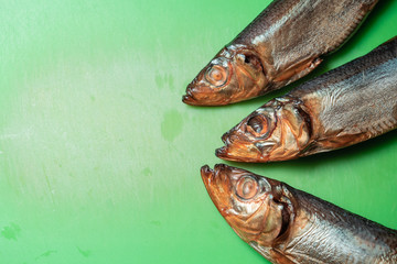 three smoked sprat fish on a green cutting board