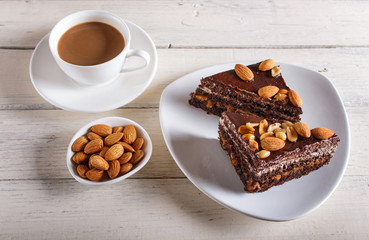 Chocolate cake with caramel, peanuts and almonds on a white wooden background.