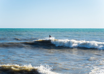 A man in a black wetsuit on the surf of the Black Sea Sochi