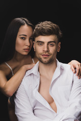 beautiful asian woman lying on shoulder of handsome boyfriend and looking at camera isolated on black