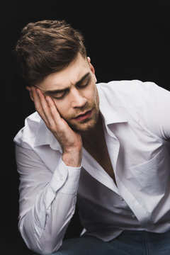 pensive handsome man in white shirt holding hand near face isolated on black