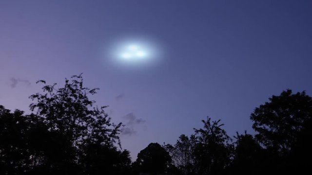 A handheld home movie video of a UFO sighting in the evening sky above the treetops. Three unidentified lights zoom across the night sky. Simulated.  	