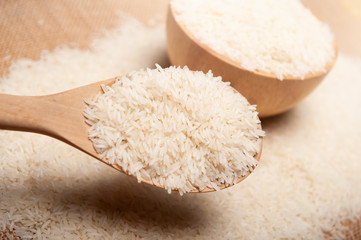 Close up view of rice in a wooden spoon and bowl on wooden background, organic and healthy concept.