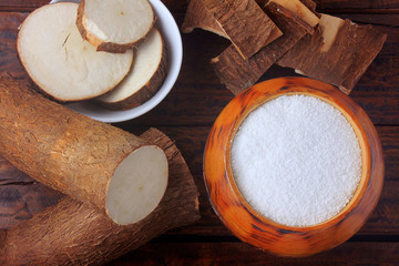 tapioca flour in wooden bowl on rustic wooden table, next to cut and sliced cassava