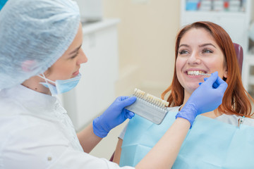 Check and select the color of the teeth in the dentist chair. Dentist makes the process of treating a beautiful young red-haired girl. Selection of a tooth implant.