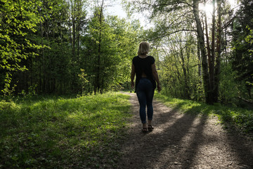 A young girl walks in the park. Spring, warm day. A girl with a good figure, blonde, in jeans and a light blouse. The trees have already dissolved the leaves. Falling shadow from the trees.