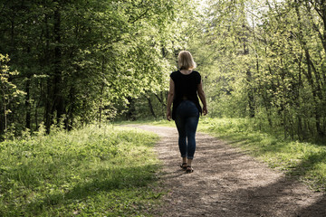 A young girl walks in the park. Spring, warm day. A girl with a good figure, blonde, in jeans and a light blouse. The trees have already dissolved the leaves. Falling shadow from the trees.