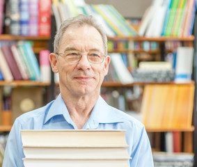 Smiling senior man holds a pile of books in the library