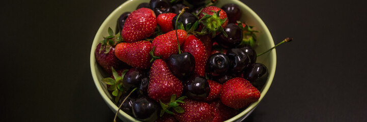 Fresh fruit of strawberries and cherries in a cup on a dark background.