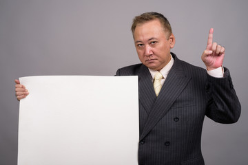 Portrait of mature Asian businessman against gray background