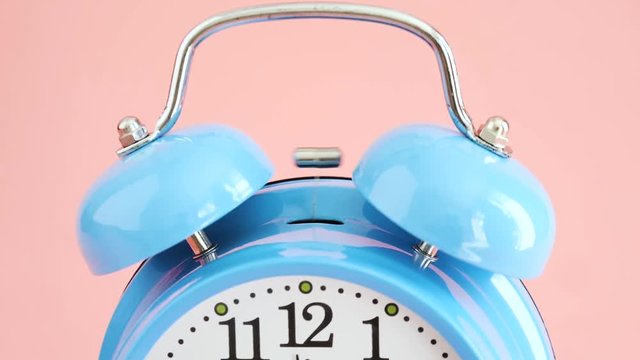 Hand stop alarm clock blue wake-up time isolated on pink background, slow motion.