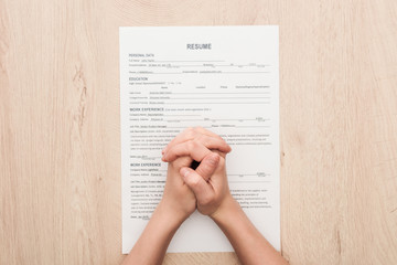 partial view of recruiter holding clenched hands on resume template on wooden table