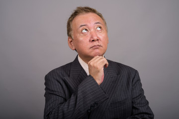 Portrait of mature Asian businessman against gray background