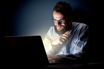 Young handsome businessman working late at night in the office with a dark background