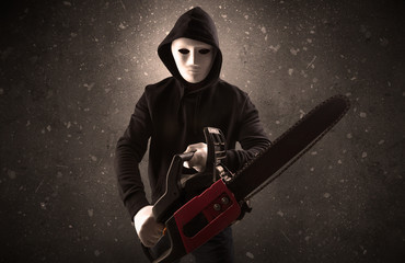 Masked armed villain in empty dark room with gun ax chainsaw mallet wrench
