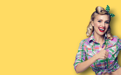 Photo of happy smiling woman, showing thumb up gesture, dressed in pin-up, over yellow background style