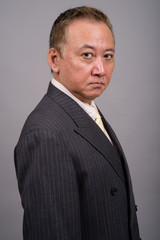 Portrait of mature Asian businessman against gray background