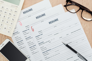 Obraz premium top view of glasses, pen, smartphone with blank screen, calculator and resume templates on wooden surface