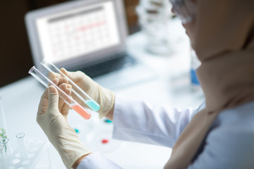 Chemist sitting near laptop and studying colorful chemical agents