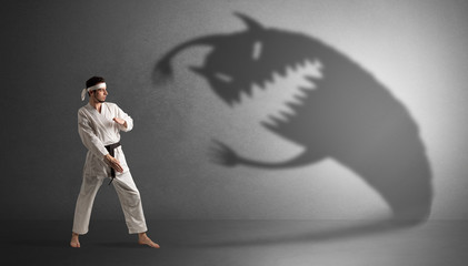 Young karate man fighting with a big black scary shadow
