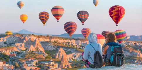 Poster Hot air balloon flying over spectacular Cappadocia - Girls watching hot air balloon at the hill of Cappadocia © muratart