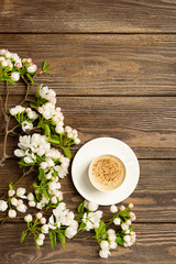 A cup of hot aromatic coffee and a blossoming branch of an apple tree on a wooden background. Flat layout.