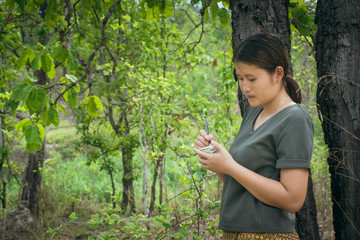 The girl is standing, taking notes in a small note book in the green forest.