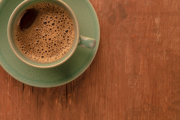 A closeup of a cup of coffee on a dark rustic wooden background, shot from the top with a place for text, toned image
