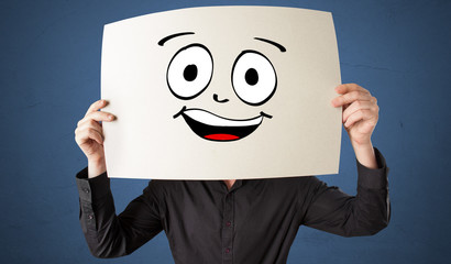Young student holding a paper with laughing emoticon in front of his face

