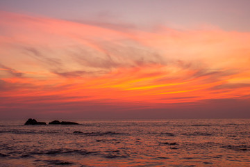 Fototapeta na wymiar ocean under bright orange clouds in a purple sunset sky