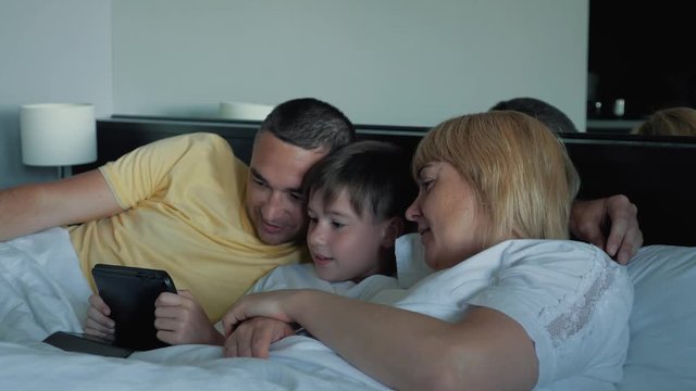 A happy family with one child lying on the bed and using a digital tablet and smartphones. Modern technologies of virtual life