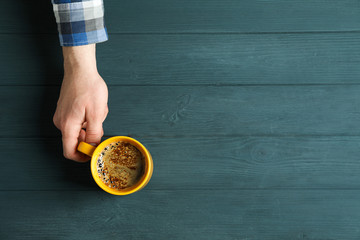 Man hand hold cup of coffee with frothy foam on wooden background, space for text and top view. Coffee time accessories