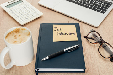 notebook with job view lettering on sticky note on wooden table with laptop, stationery, glasses and cup of coffee