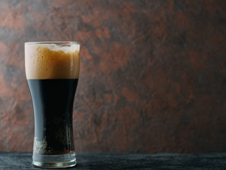 Craft dark beer porter in a glass on a brown dark background with copyspace