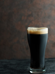 Craft dark beer porter in a glass on a brown dark background with copyspace