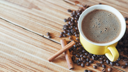 Yellow coffee Cup with cinnamon and coffee beans on wooden table and copy space