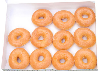 Top view flat lay of plain glazed donuts in a white box isolated. One dozen minus one donut. The original glazed donut has remained peoples favorite throughout history.