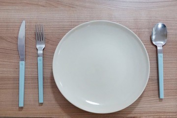 Top view of empty plate with fork, spoon and knife on wooden table in restaurant