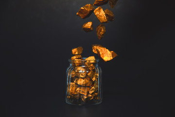 Falling gold nuggets or gold ore and glass jar in dark room