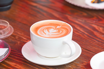 Coffee cup latte art (heart) in cafe on wooden red table