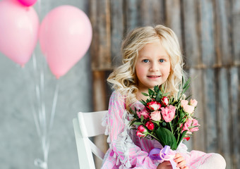 Beautiful little girl with blond hair and a bouquet of fresh flowers in a bright studio. Daylight