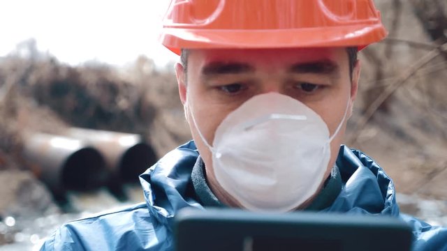 Environmental pollution. A man in a helmet and respirator with a tablet measures the level of pollution of waste water from a pipe. Environmental conservation concept