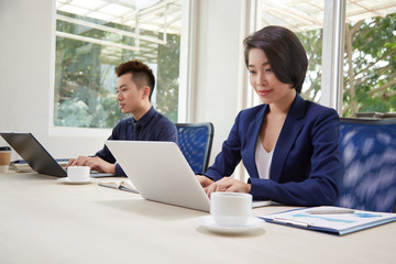 Asian business people sitting at the table and typing on laptop computers, they working online and communicating with clients during their work day at office