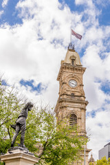 Fototapeta na wymiar The statue of Captain Charles Sturt Explorer and the Victoria Tower of Adelaide against a beautiful blue sky with some clouds, Southern Australia