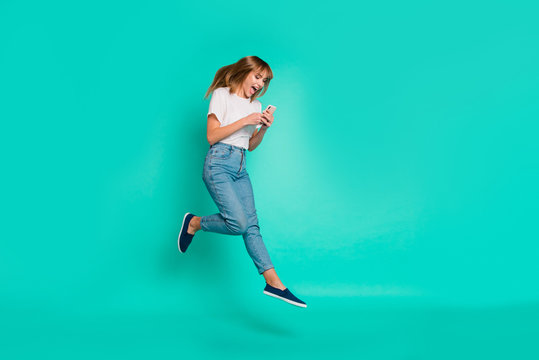 Full Length Side Profile Body Size Photo Beautiful She Her Lady Weekend Vacation Jump High Arms Hands Hold Telephone Smart Phone Achieve Wear Casual Jeans Denim White T-shirt Isolated Teal Background