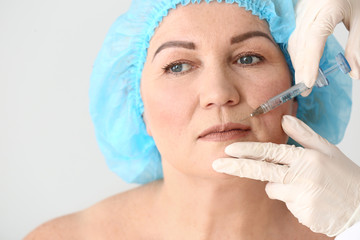 Mature woman receiving injection in face on light background