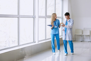 Male doctor and female medical assistant walking down the corridor in clinic - Powered by Adobe