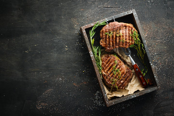 Grilled ribeye beef steak, herbs and spices on a dark table. Top view. Free space for your text.