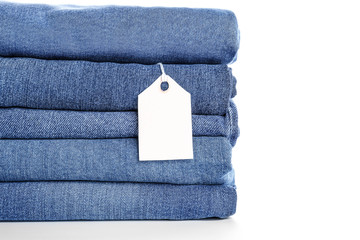 Stack of jeans pants with shopping tag on white background